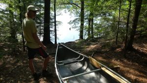 picture of a man beside a canoe while backcountry camping on a portage with paddles and fishing rods rigged inside the canoe with bungee cords