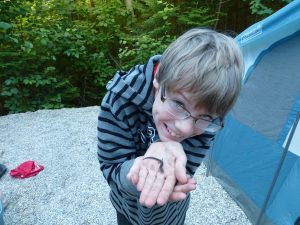 picture of a boy holding a salamander in his dirty hands while camping