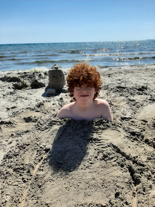 picture of a boy buried up to his neck in sand at Presqu'ile Provincial Park beach