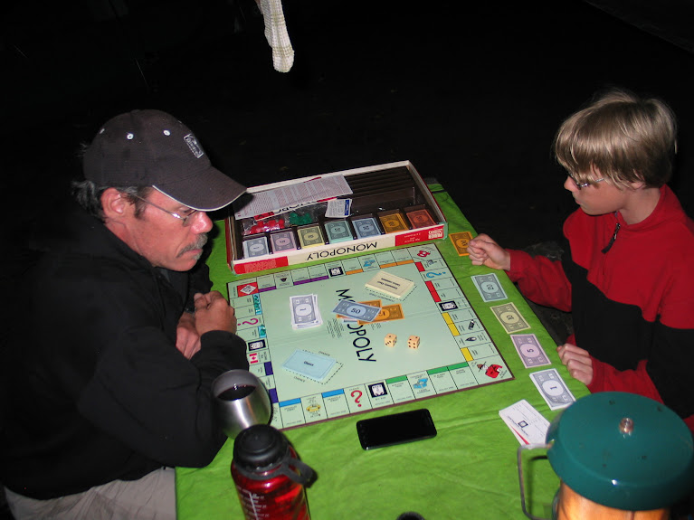 picture of Tim and Thomas playing the board game monopoly by the light of the Coleman lantern while camping 