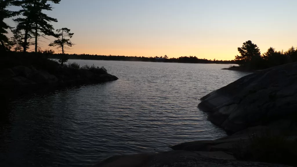 picture of a backcountry camping sunset on a tranquil lack with trees and rocks