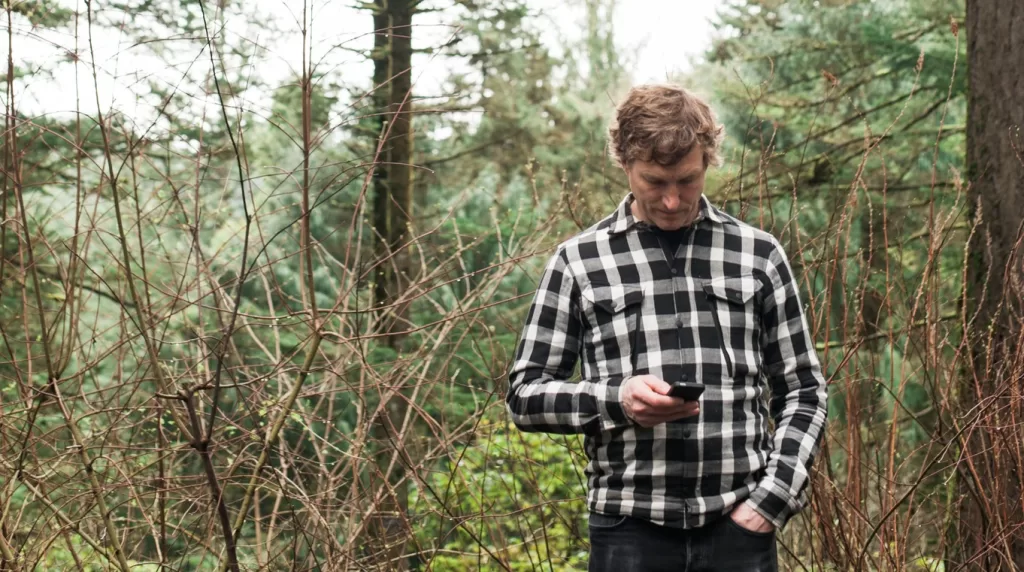picture of a man in a forest looking at his cellphone, wanting to contact the Super Good Camping Podcast